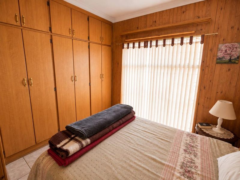 A bedroom featuring extensive built-in wooden cabinetry, timber wall paneling, and vertical blinds, offering a dated but functional living space.