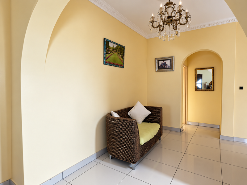 A bright hallway featuring arched architectural transitions, decorative crown molding, polished tile flooring, and an elegant crystal chandelier.