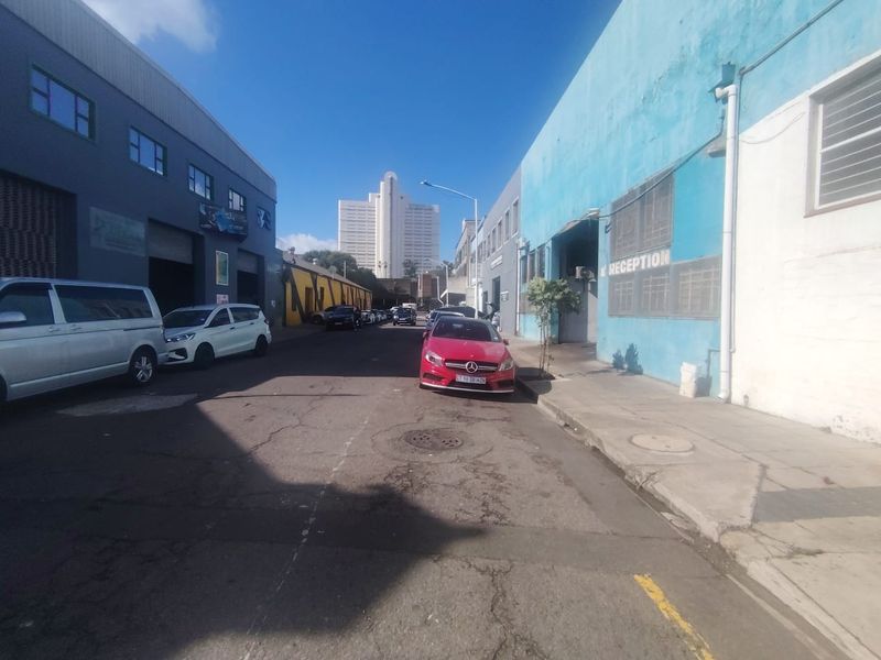 Street view of an industrial precinct featuring commercial warehouse buildings with roller shutter doors and weathered exterior finishes.