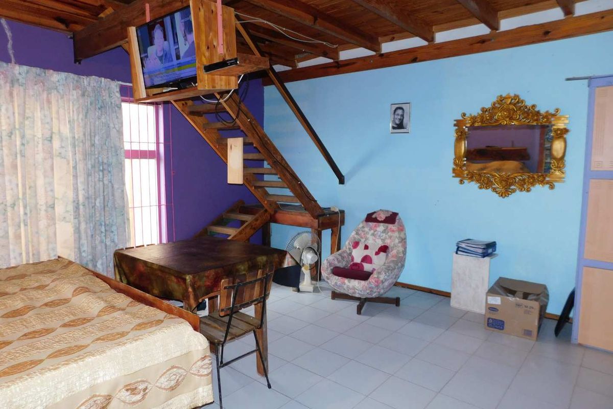 A multi-level living space featuring exposed timber ceiling beams, tiled flooring, and a wooden staircase leading to an upper level.