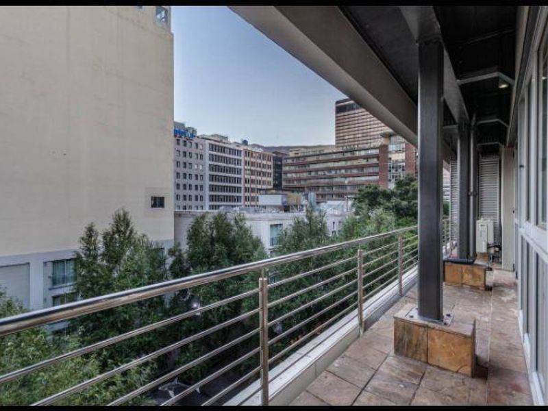 A spacious balcony featuring tiled flooring, a stainless steel balustrade, and steel support columns, offering an urban city view.