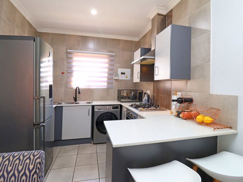 Modern kitchen featuring stone countertops, built-in cabinetry, gas hob with extractor, and tiled finishes, offering a functional and well-maintained cooking space.