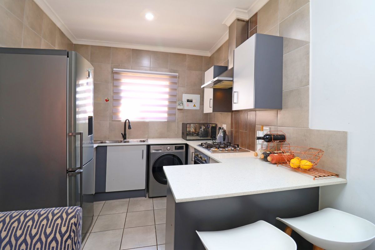 Modern kitchen featuring stone countertops, built-in cabinetry, gas hob with extractor, and tiled finishes, offering a functional and well-maintained cooking space.