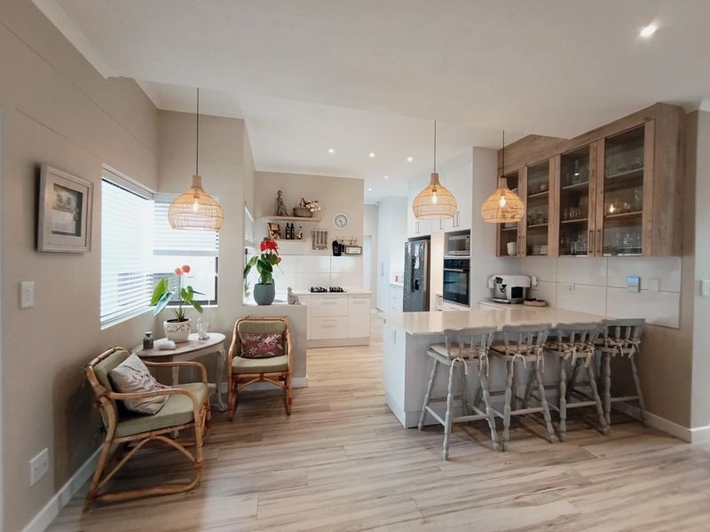 Modern open-plan kitchen featuring a central island, stone countertops, built-in appliances, and elegant glass-fronted cabinetry, seamlessly integrated with a bright dining area.