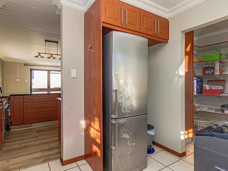 A functional scullery area featuring built-in cabinetry, tiled flooring, and an adjacent walk-in pantry with open shelving, providing additional storage and utility space.