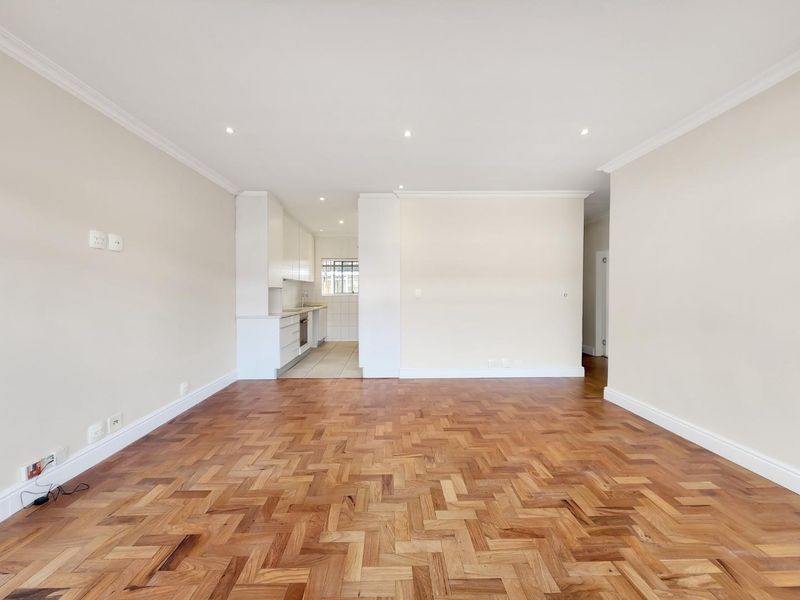 Spacious open-plan living area featuring beautiful herringbone parquet flooring, recessed lighting, and a compact, functional kitchen with built-in cabinetry and integrated appliances.