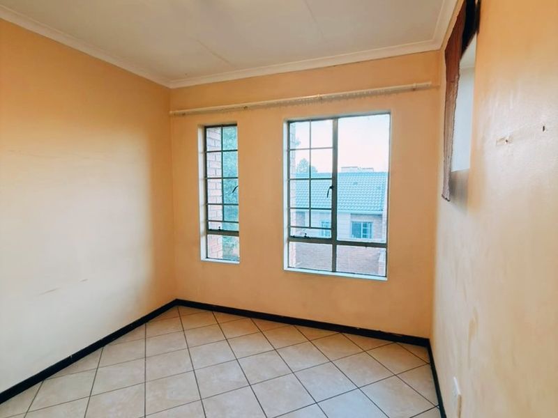 An empty bedroom featuring tiled flooring, steel-framed windows, and neutral wall finishes, offering a blank canvas for personalization.