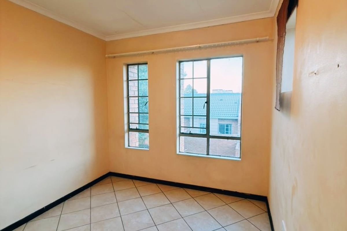 An empty bedroom featuring tiled flooring, steel-framed windows, and neutral wall finishes, offering a blank canvas for personalization.