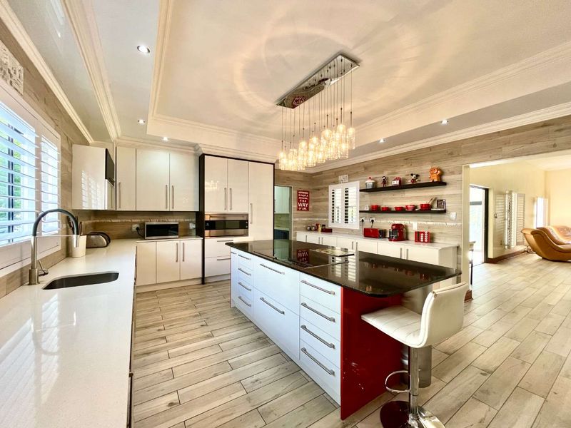Modern kitchen featuring a large central island with stone countertops, integrated appliances, shaker cabinetry, and elegant tray ceiling lighting.