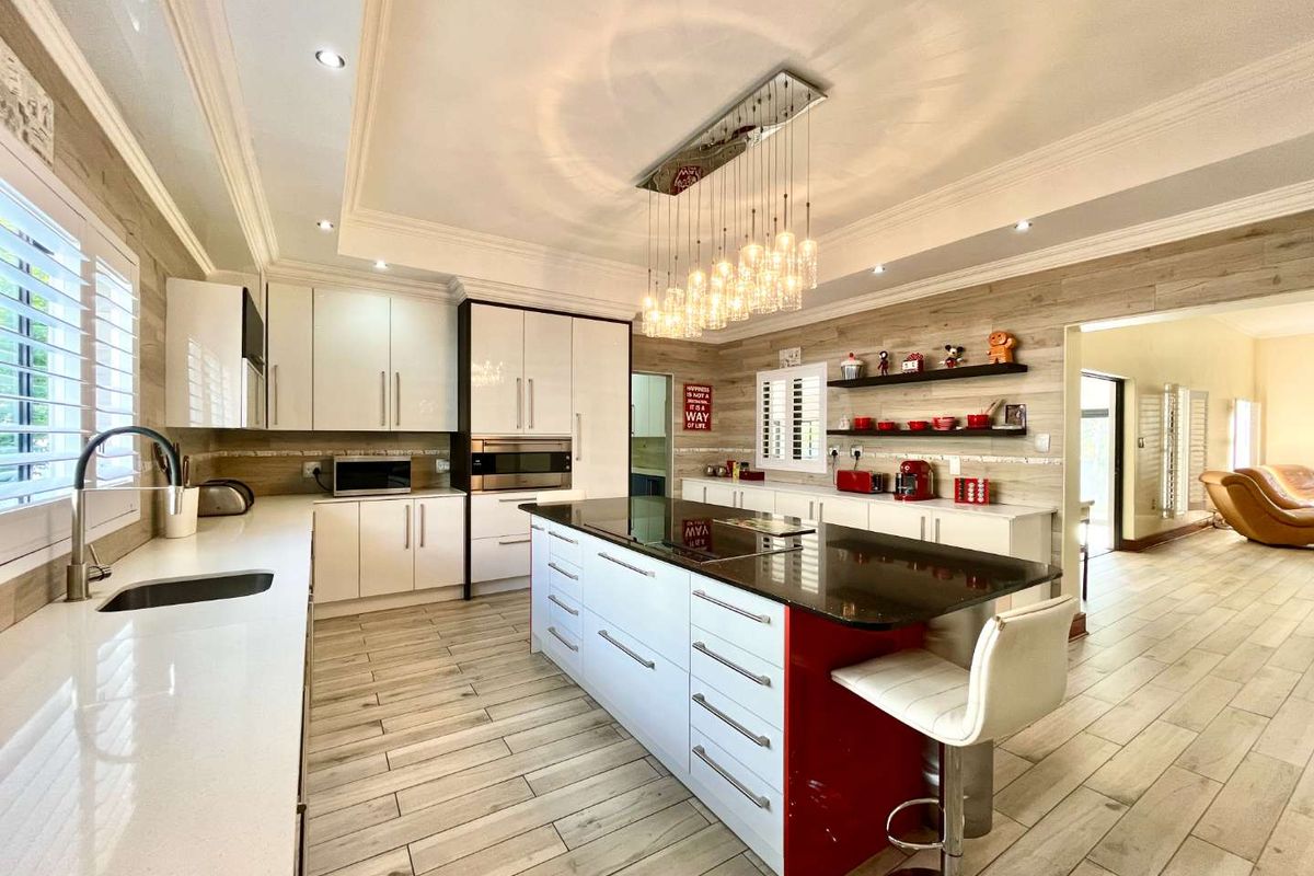Modern kitchen featuring a large central island with stone countertops, integrated appliances, shaker cabinetry, and elegant tray ceiling lighting.