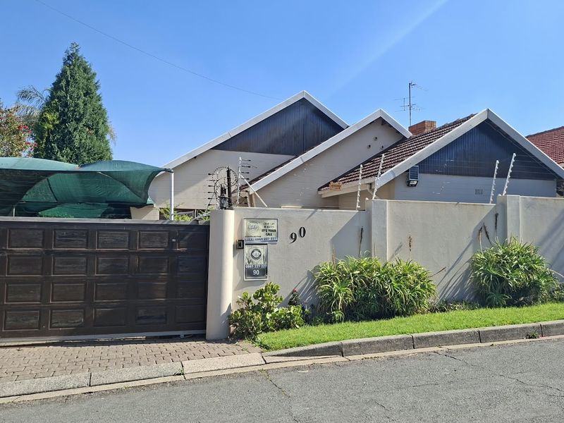 Front exterior view of the property featuring a paved driveway, secure perimeter wall with electric fencing, and a sliding gate.