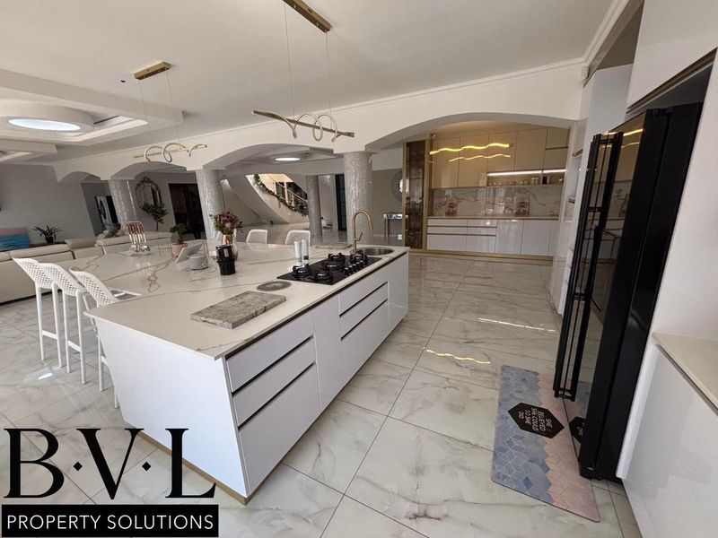 Spacious open-plan kitchen featuring a large central island with gas cooktop, premium marble-look flooring, and elegant architectural archways connecting to the living area.