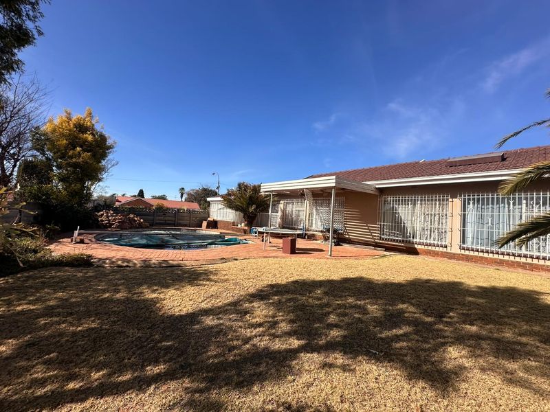 Rear exterior view featuring a swimming pool, paved patio area, and a covered veranda attached to the main house structure.