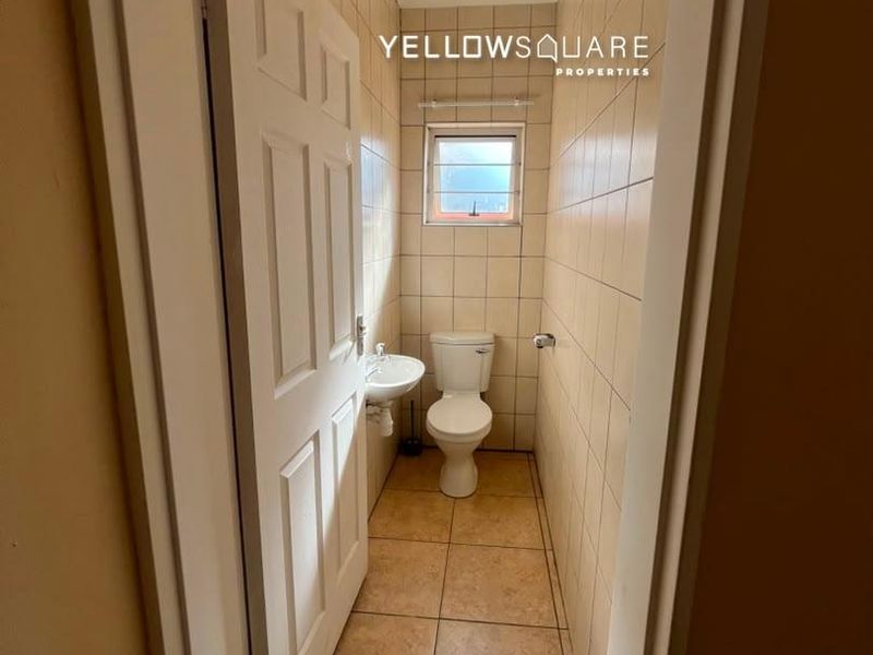 A compact guest bathroom featuring tiled walls and flooring, a wall-mounted basin, and a standard toilet.