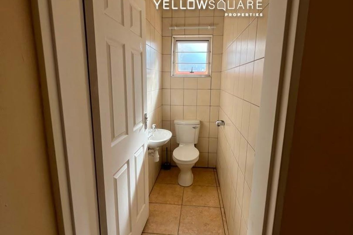 A compact guest bathroom featuring tiled walls and flooring, a wall-mounted basin, and a standard toilet.