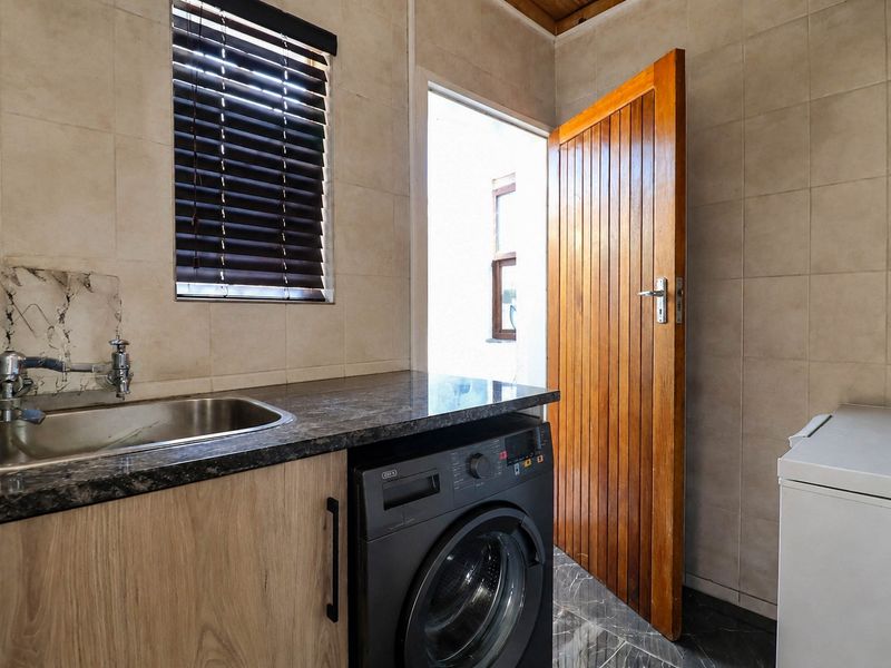 A functional laundry room featuring tiled walls and flooring, a stainless steel sink with laminate countertop, and built-in cabinetry.