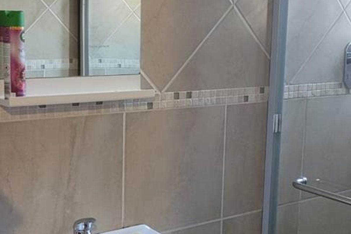 A functional bathroom featuring a vanity cabinet with basin, wall-mounted mirror, and a glass-enclosed shower with neutral wall tiling.