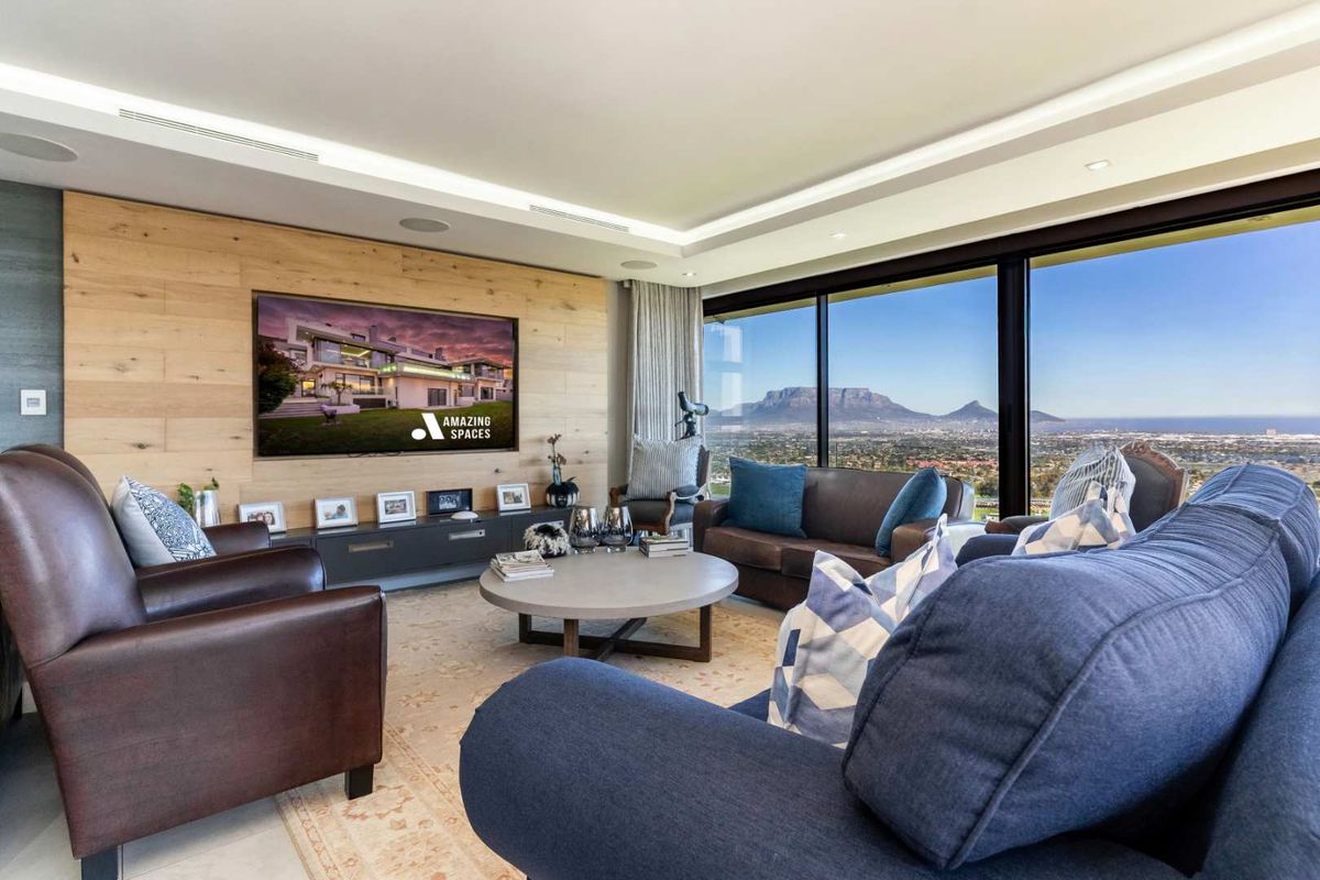 Modern living room featuring floor-to-ceiling sliding glass doors with panoramic mountain and city views, recessed ceiling lighting, and a feature timber-clad wall.