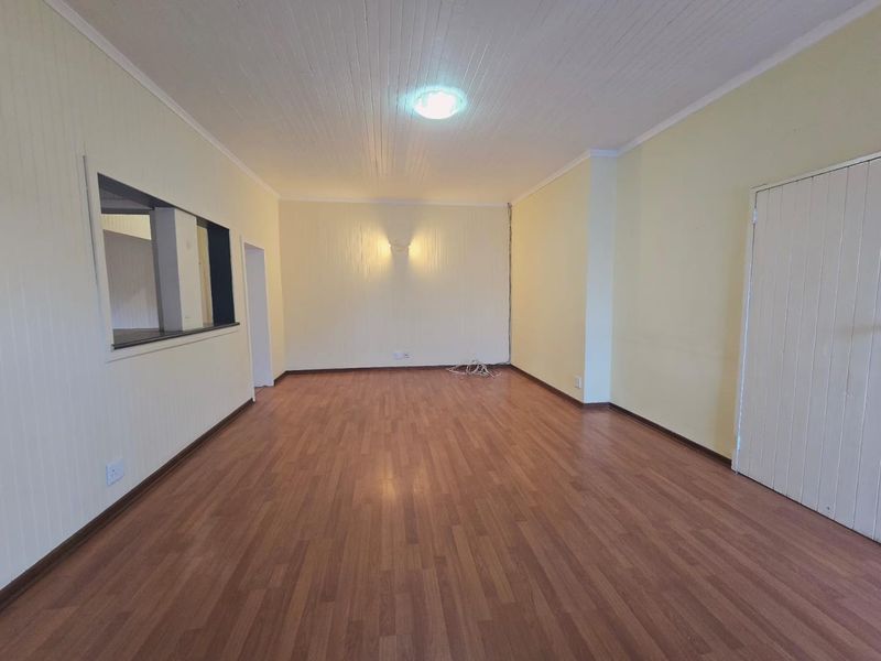 A spacious, empty living room featuring laminate flooring, a tongue and groove ceiling, and a convenient serving hatch connecting to the kitchen area.