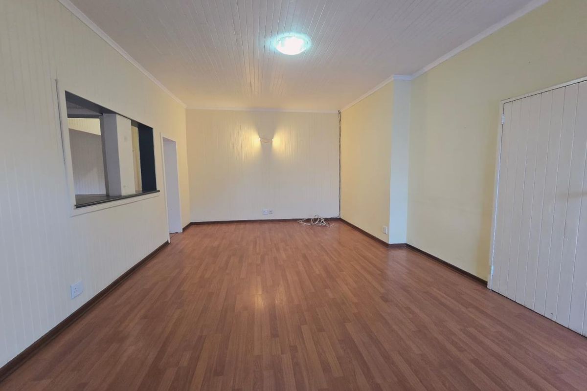 A spacious, empty living room featuring laminate flooring, a tongue and groove ceiling, and a convenient serving hatch connecting to the kitchen area.