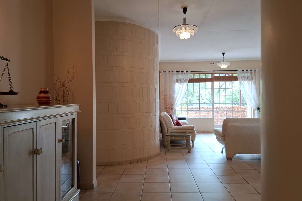 Spacious living area featuring a distinctive curved brick feature wall, tiled flooring, and large windows providing natural light and access to the outdoor space.