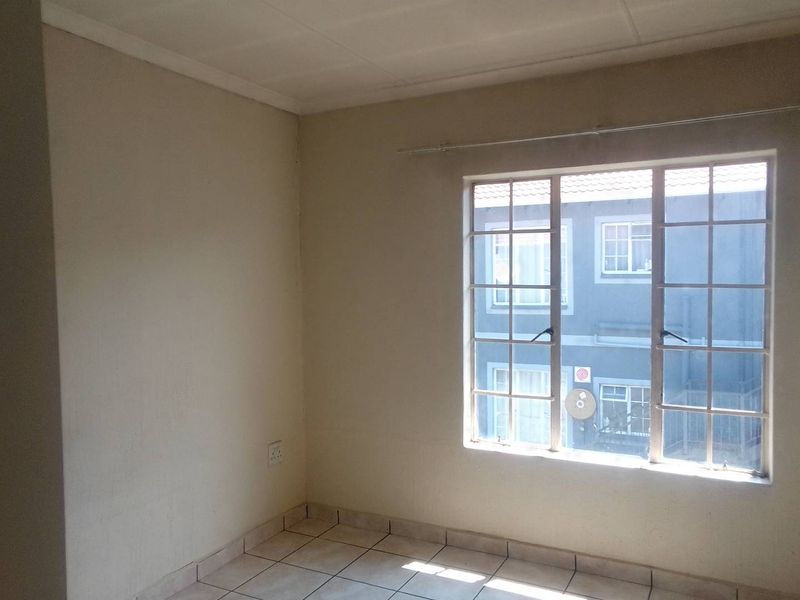 An empty bedroom featuring tiled flooring, a window with security bars, and neutral wall finishes, offering a blank canvas for personalization.