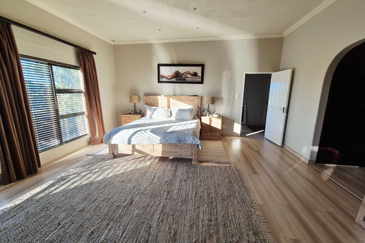Spacious bedroom featuring light wood-look flooring, large window with blinds, and an arched doorway leading to an adjacent room.