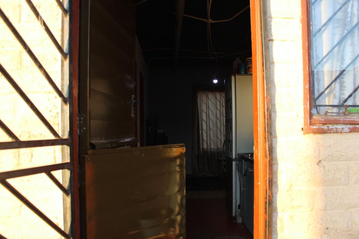 View through a stable door into a dimly lit kitchen area featuring exposed ceiling beams and basic cabinetry.