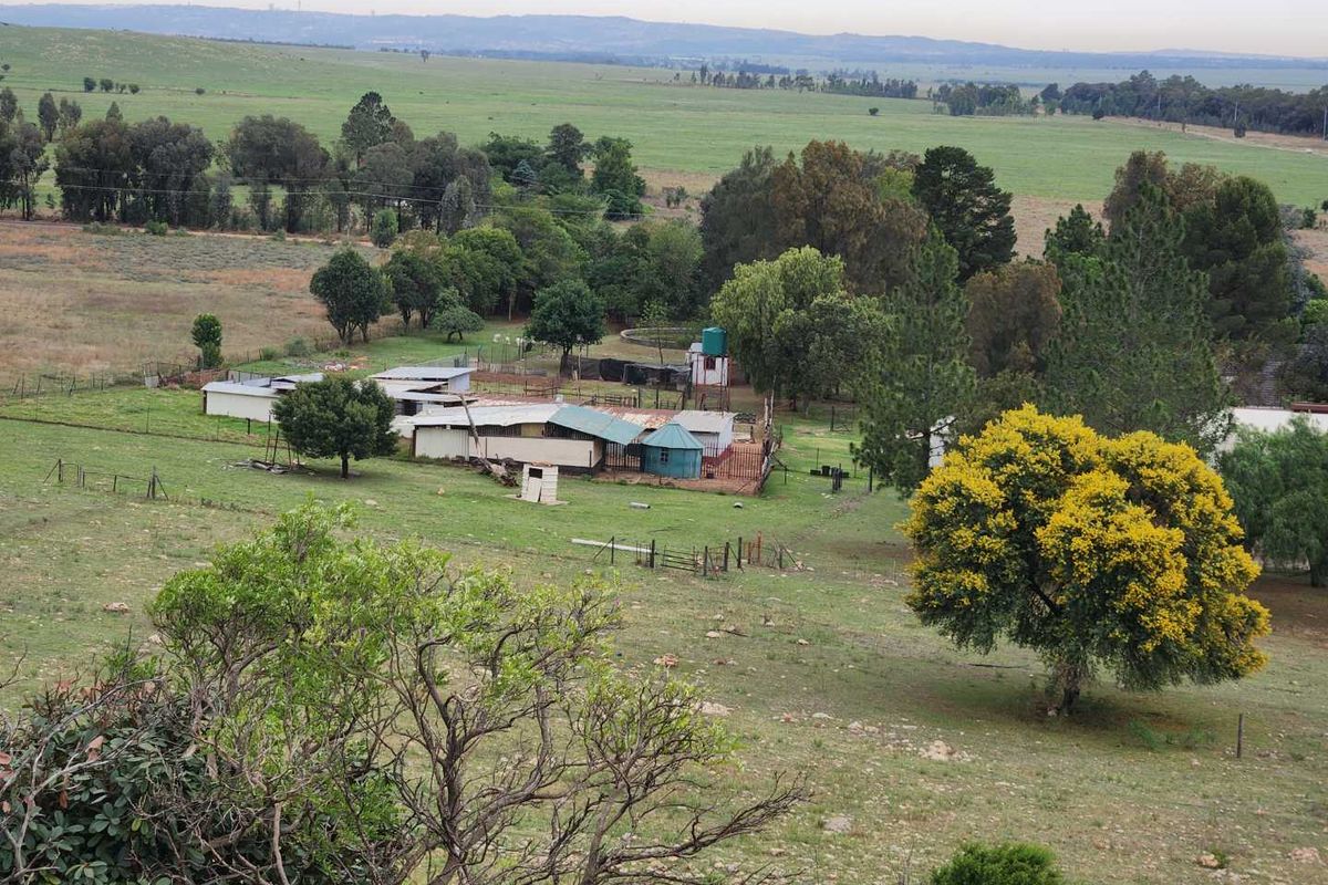 An elevated aerial view of a rural property featuring multiple outbuildings, a water tank, and expansive surrounding farmland.