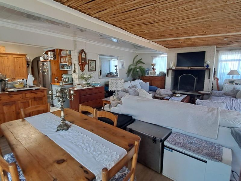 Spacious open-plan living and dining area featuring a rustic timber beam ceiling and a traditional brick fireplace.
