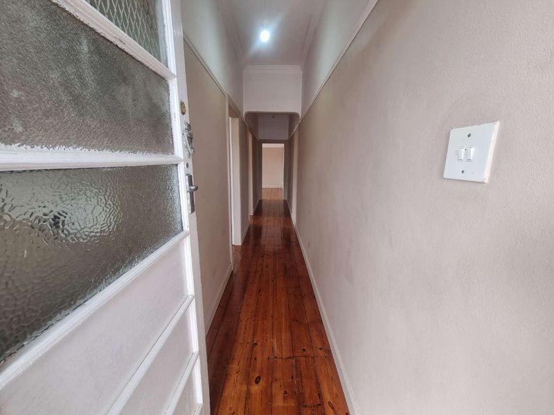 A long, empty hallway featuring polished hardwood flooring and neutral wall finishes, providing access to multiple rooms within the property.