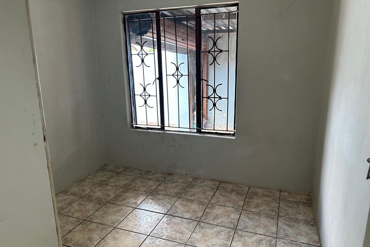A small, empty bedroom featuring tiled flooring and a window fitted with security burglar bars.