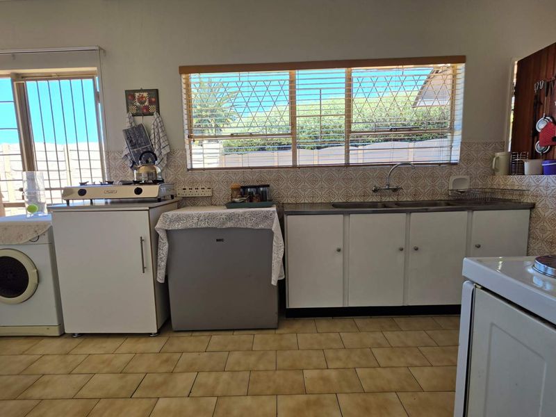 A functional kitchen featuring dated cabinetry, tiled backsplash, and tiled flooring, with large windows providing natural light and security bars.