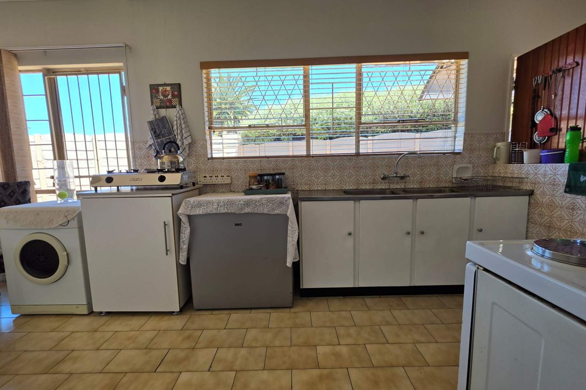 A functional kitchen featuring dated cabinetry, tiled backsplash, and tiled flooring, with large windows providing natural light and security bars.