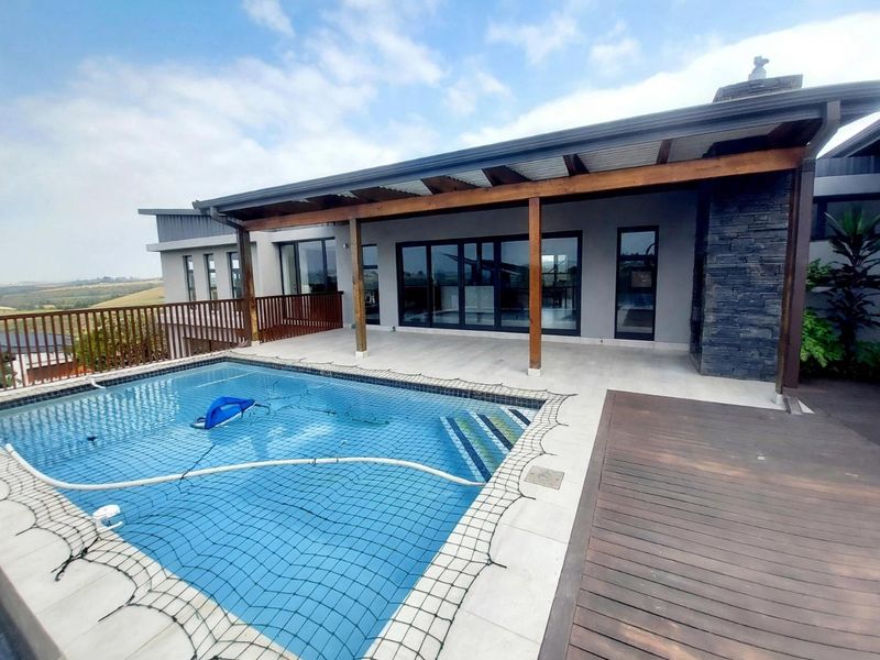Outdoor entertainment area featuring a swimming pool with safety net, timber decking, and a covered patio with stone-clad fireplace feature.
