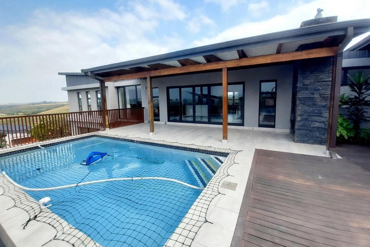Outdoor entertainment area featuring a swimming pool with safety net, timber decking, and a covered patio with stone-clad fireplace feature.