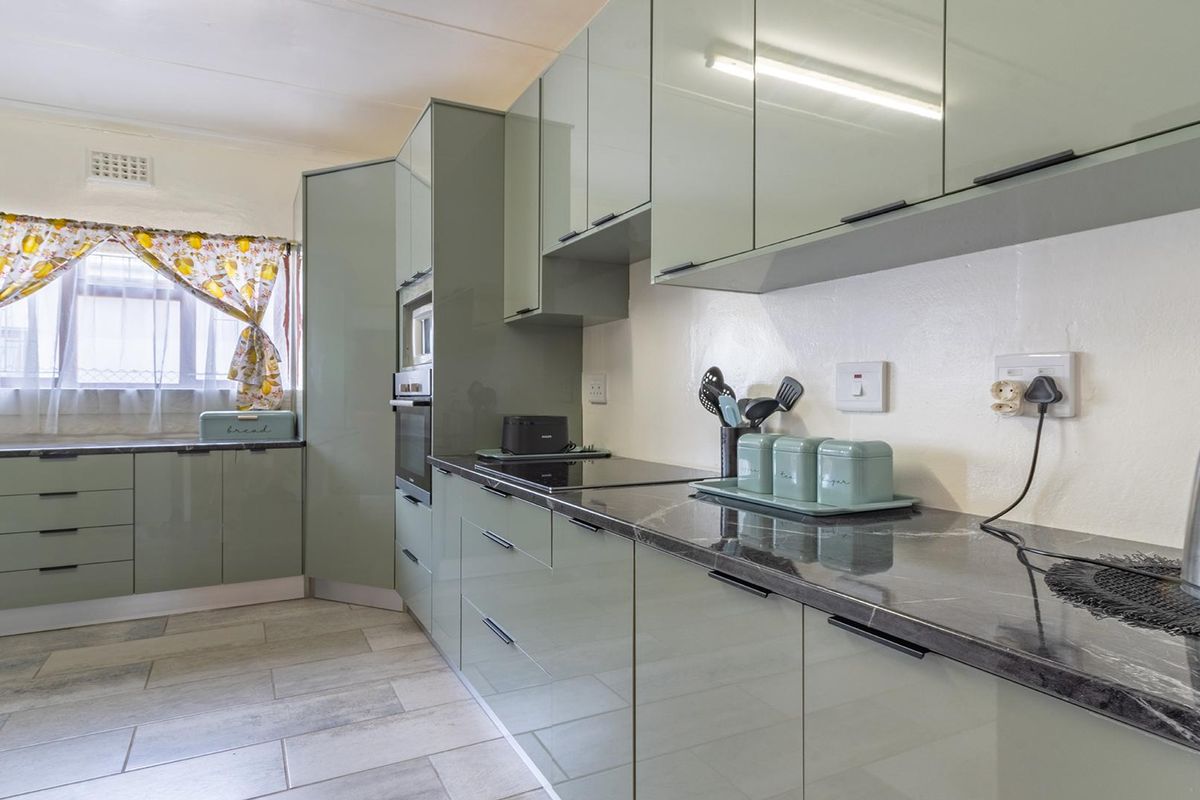 Modern kitchen featuring sage green cabinetry, dark stone-look countertops, integrated oven, and sleek tiled flooring.