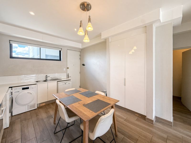 A functional laundry area featuring built-in cabinetry, a stainless steel sink, tiled splashback, and integrated appliances, finished with modern tiled flooring.