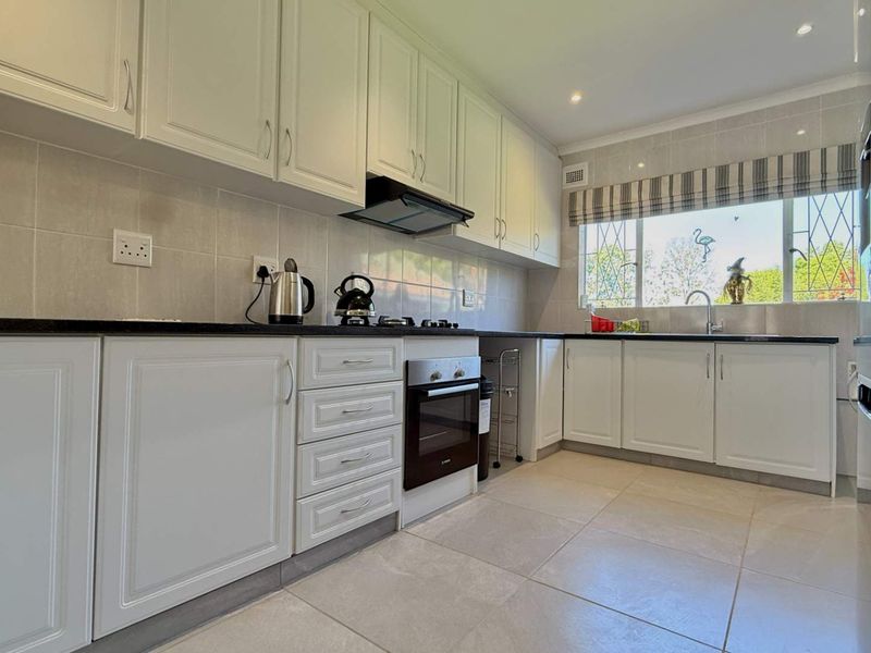 A well-maintained kitchen featuring white cabinetry, dark stone countertops, built-in oven, gas hob, and tiled finishes with ample natural light.