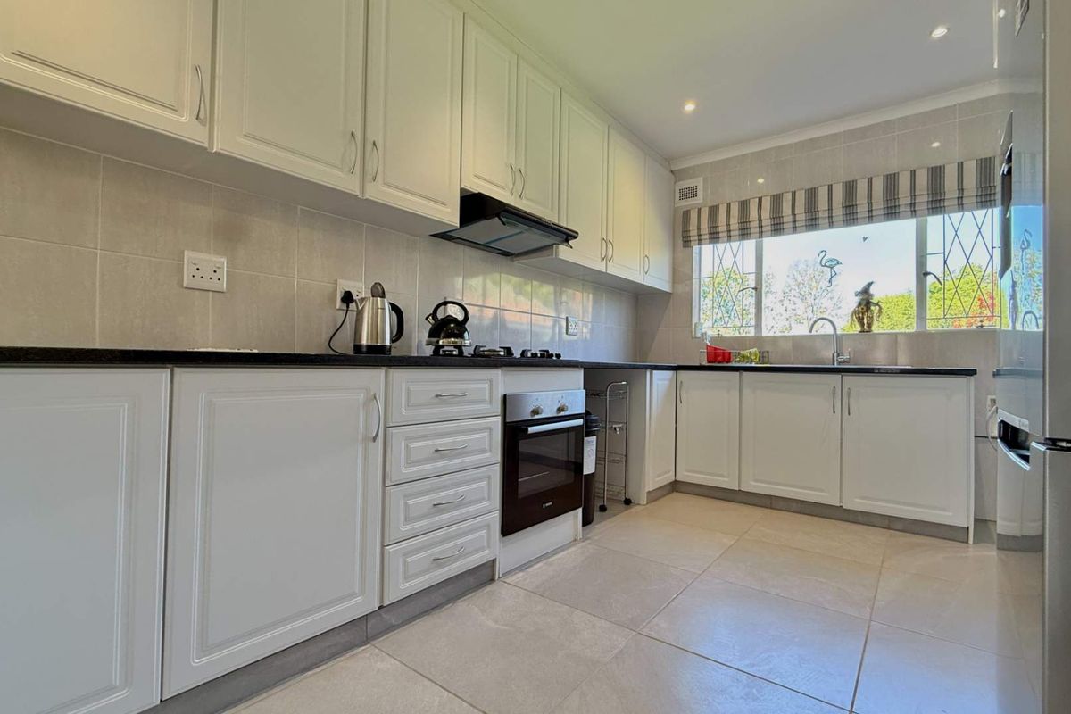 A well-maintained kitchen featuring white cabinetry, dark stone countertops, built-in oven, gas hob, and tiled finishes with ample natural light.