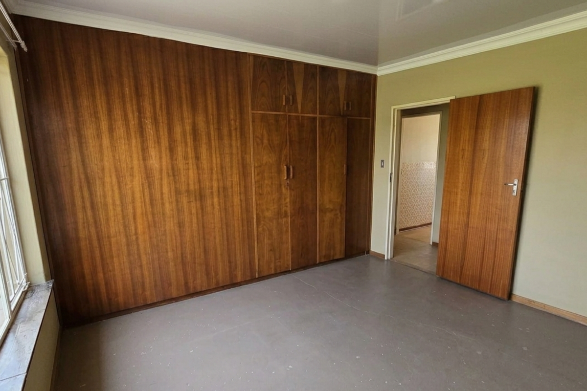 A bedroom featuring built-in wooden cupboards, large windows with security bars, and a neutral interior finish.