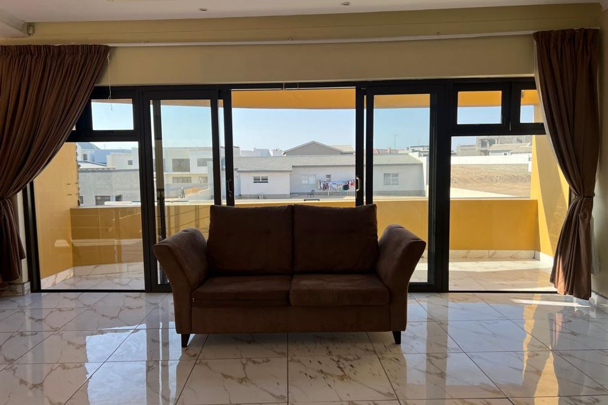 A bright living area featuring large sliding glass doors that open onto a private balcony, finished with polished marble-look floor tiles.
