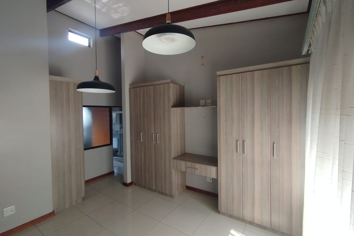 Spacious bedroom featuring neutral tiled flooring, exposed timber ceiling beams, and extensive built-in cupboard storage with an integrated vanity area.