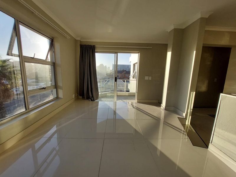 Bright and spacious open-plan living area featuring polished porcelain floor tiles, large windows, and direct access to a private balcony.