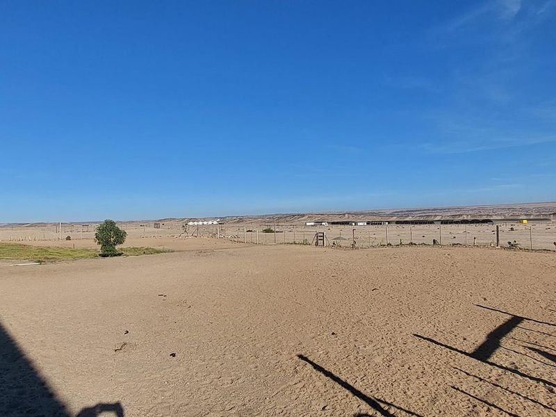 Expansive view of the surrounding arid landscape and open land, featuring perimeter wire fencing and a clear horizon line.