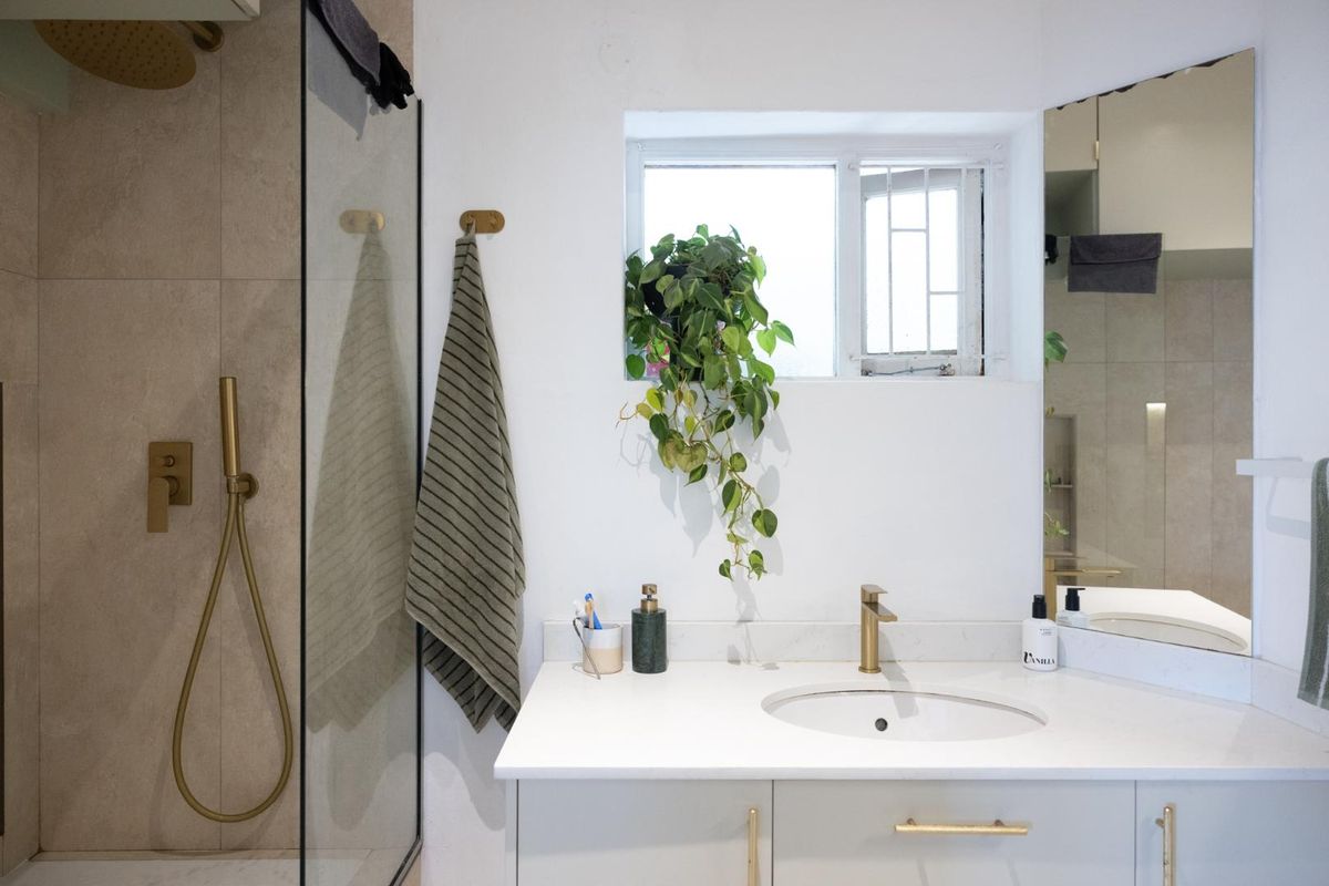 Modern bathroom featuring a vanity with stone countertop, brass fixtures, and a glass-enclosed shower with a rainfall shower head.