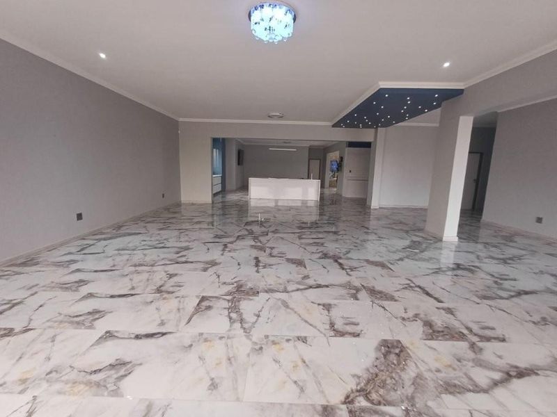 Spacious open-plan living area featuring polished marble-look tiled flooring, modern recessed lighting, and a unique decorative ceiling feature.