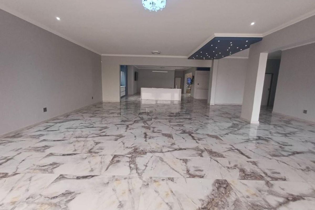 Spacious open-plan living area featuring polished marble-look tiled flooring, modern recessed lighting, and a unique decorative ceiling feature.