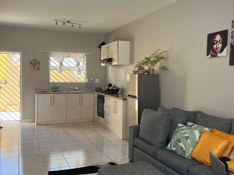 Open-plan living area featuring a functional kitchen with built-in cabinetry, oven, and extractor fan, seamlessly connected to the lounge space with tiled flooring.