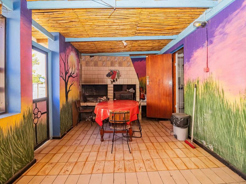 Covered outdoor patio area featuring a built-in braai, tiled flooring, and a rustic thatched ceiling, offering a functional space for outdoor entertaining.